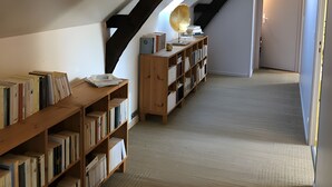 A spacious attic room with sloped ceilings, wooden bookshelves, and a unique light fixture. - Gîte Bonaty – Comfortable, Quiet, Cozy Furnished Home for 2 to 9 Guests (Soulgé-sur-Ouette)