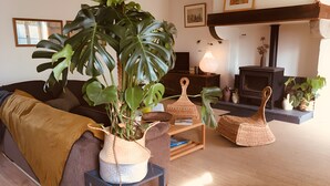 A living room with a sofa, a large potted plant, wicker baskets, a fireplace, and framed pictures on the wall. - Gîte Bonaty – Comfortable, Quiet, Cozy Furnished Home for 2 to 9 Guests (Soulgé-sur-Ouette)