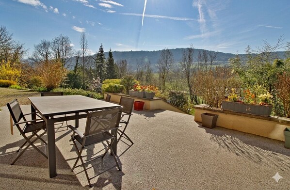 An outdoor patio with a table and chairs, surrounded by potted plants and a scenic view of mountains.
