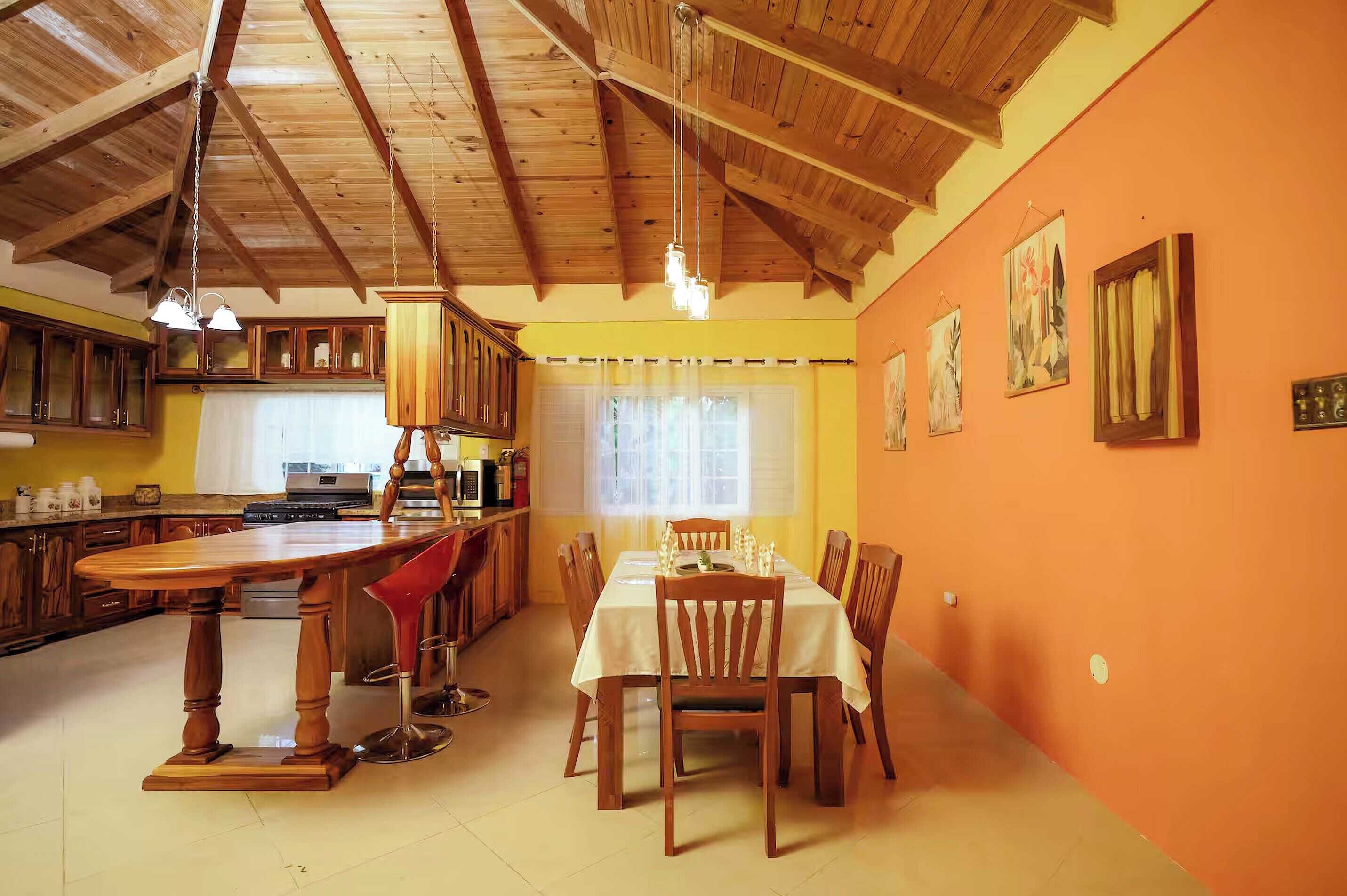 A dining area with a wooden table and chairs, a kitchen with wooden cabinets, and a ceiling with exposed beams.
