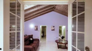 An open door to a living room with a high ceiling, a brown leather sofa, a glass coffee table, and a hallway leading to another room. - Paradise Oasis (Tower Isle)