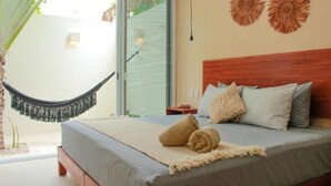 Un dormitorio con cama, almohadas, una colcha, una hamaca y una pared decorada.