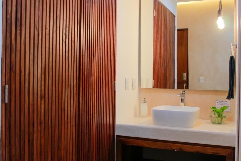 Ein Badezimmer mit einer Wand aus Holzpaneelen, einem weißen Waschbecken, einem Spiegel und einer hängenden Glühbirne.