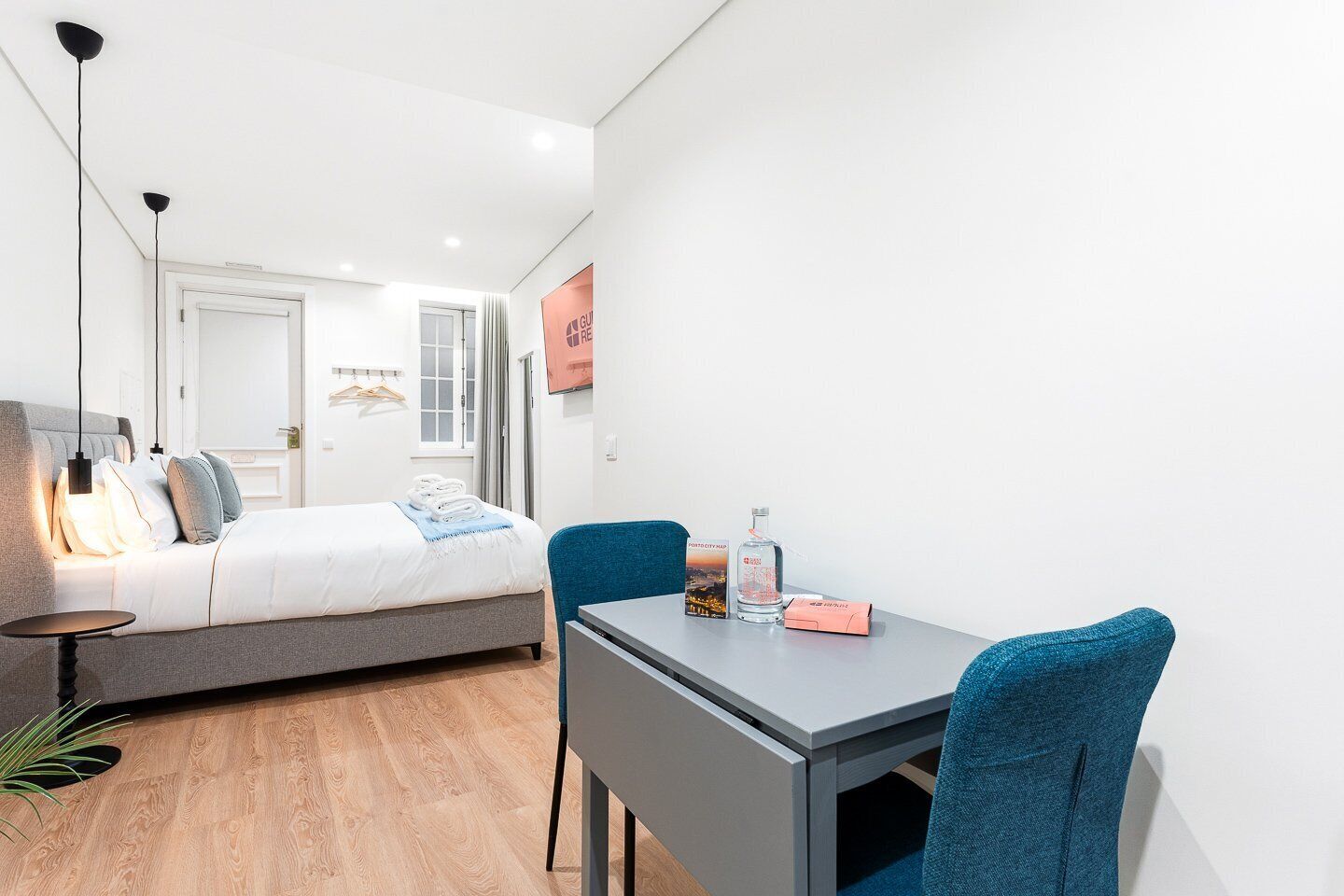 A modern hotel room with a bed, bedside table, and a desk with a chair.