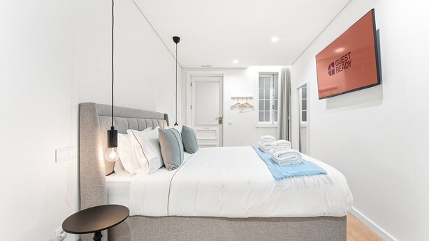 Moderni hotellihuone, jossa on suuri sänky, yöpöytä, riippuvalaisin ja seinälle kiinnitetty kyltti.