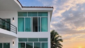 A modern two-story house with a swimming pool, large windows, and a view of the ocean at sunset. - Duplex w/pool+Bay & Sunset Views by Zona Romantica (Puerto Vallarta)