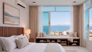A hotel room with a large bed, a window seat with books, and a view of the sea. - Duplex w/pool+Bay & Sunset Views by Zona Romantica (Puerto Vallarta)