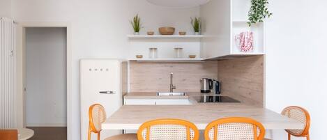 A modern kitchen with a wooden island, white cabinetry, and orange chairs.