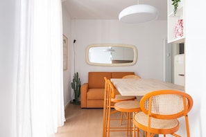 Ein moderner Essbereich mit einem Holztisch, orangefarbenen Stühlen, einer weißen Pendelleuchte und einem Spiegel an der Wand.