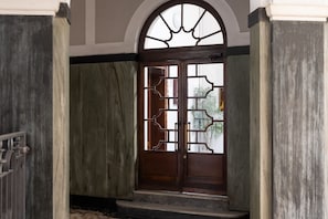 Eine Holztür mit aufwendischer Metallverzierung, die zu einem Raum mit Marmorboden und weißer Decke führt.