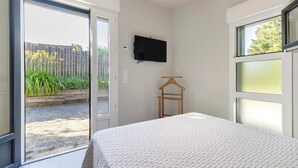 A bedroom with a bed, a TV mounted on the wall, a wooden hanger, and a sliding glass door leading to an outdoor area. - Charming 3-Star House with Heated Saltwater Pool and Private Garden (Sarlat-la-Canéda)