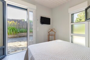 Ein Schlafzimmer mit einem Bett, einem an der Wand montierten Fernseher, einem Holzkleiderbügel und einer Glastür, die zu einem Außenbereich führt.
