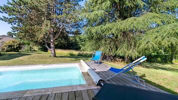 Una terrazza in legno con piscina, sedie a sdraio e alberi.