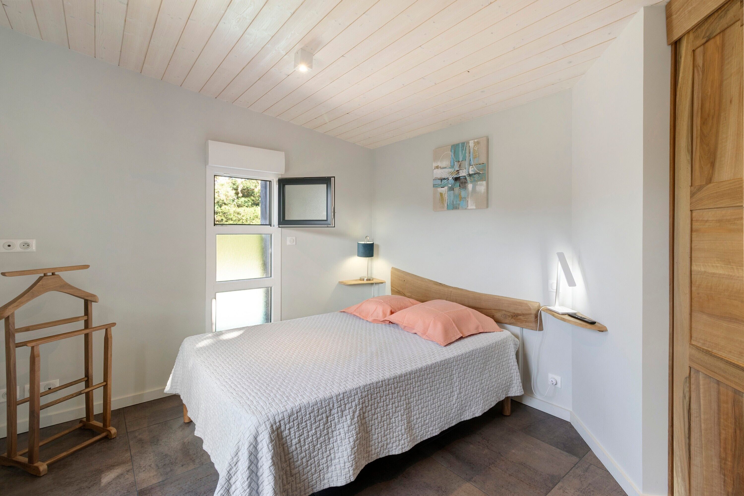A bedroom with a bed, bedside table, lamp, and a wooden hanger rack.