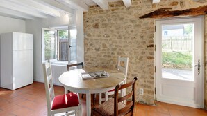 A stone wall, a white door, a white table with chairs, and a white refrigerator. - Charming 3-Star House with Heated Saltwater Pool and Private Garden (Sarlat-la-Canéda)