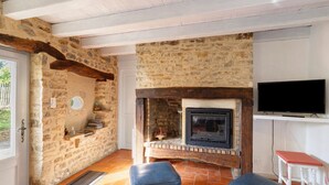 A stone-walled room with a fireplace, a television mounted above it, and a door leading outside. - Charming 3-Star House with Heated Saltwater Pool and Private Garden (Sarlat-la-Canéda)