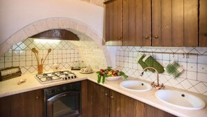 Een keuken met een stenen boog, houten kastjes, een gasfornuis en een dubbele spoelbak.