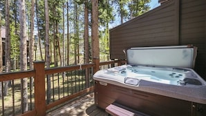 Een hottub op een houten terras met uitzicht op hoge bomen.