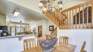 Een eethoek met een houten tafel, stoelen en een decoratieve schaal als middelpunt. Een trap met houten leuningen is zichtbaar op de achtergrond.