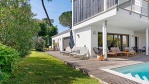 Ett modernt hus med en träaltan, utomhusmöbler och en swimmingpool.