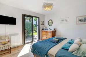 Une chambre à coucher comprenant un lit, une commode en bois, un téléviseur et une porte-fenêtre coulissante donnant sur un espace extérieur.
