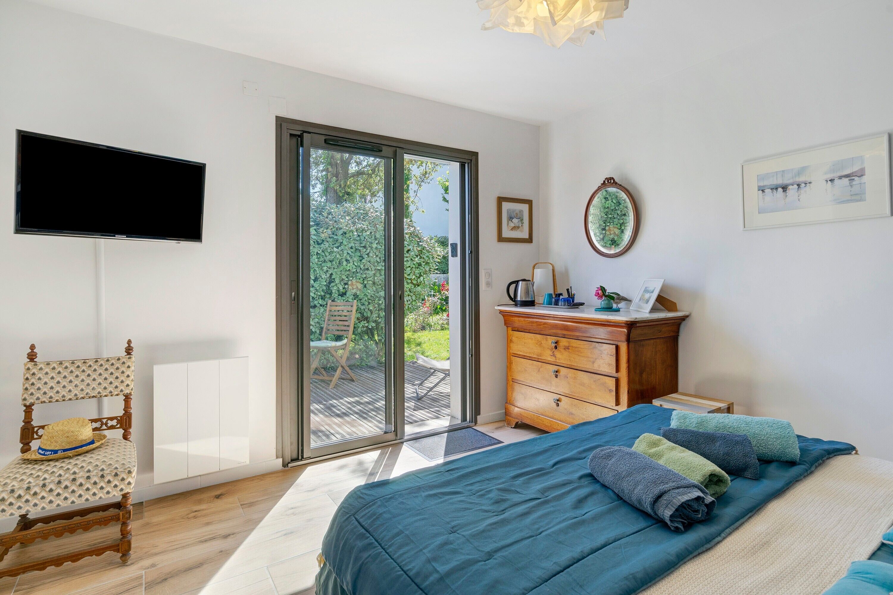 Une chambre à coucher comprenant un lit, un téléviseur, une commode en bois, une chaise et une porte-fenêtre coulissante donnant sur un espace extérieur.