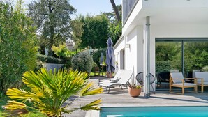 A poolside area with lounge chairs, a palm tree, and a modern building with large windows. - Charming Room with Pool and Garden – Breakfast Included (Saint-Palais-sur-Mer)