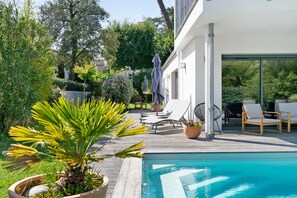 A poolside area with lounge chairs, a palm tree, and a modern building with large windows. - Charming Room with Pool and Garden – Breakfast Included (Saint-Palais-sur-Mer)