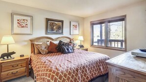 A bedroom with a large bed, two bedside tables, a desk, and a window with a view of trees. - New Listing! Ski In/Walk to the Lift/Town (Breckenridge)