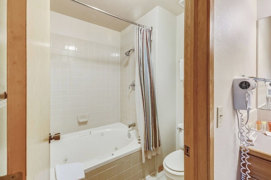A bathroom with a bathtub, shower curtain, toilet, and a hairdryer on a counter.
