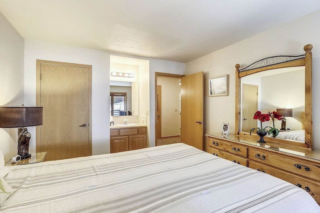 A bedroom with a bed, a dresser, a mirror, and a bathroom visible through an open door.