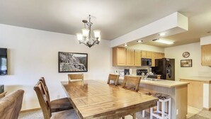 A modern kitchen with wooden cabinets, a central island, and a dining area with a wooden table and chairs. - New Listing! Ski In/Walk to the Lift/Town (Breckenridge)