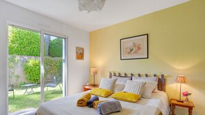 A bedroom with a bed, pillows, a nightstand, a lamp, and a view through a sliding door to an outdoor area. - Cozy Room with Terrace and Pool – Breakfast Included (Saint-Palais-sur-Mer)