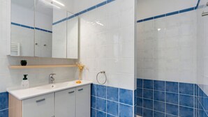 A bathroom with white and blue tiles, a sink with a mirror, a towel ring, and a small shelf with toiletries. - Cozy Room with Terrace and Pool – Breakfast Included (Saint-Palais-sur-Mer)