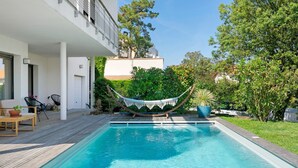 A swimming pool with a hammock, wooden deck, and outdoor furniture. - Cozy Room with Terrace and Pool – Breakfast Included (Saint-Palais-sur-Mer)