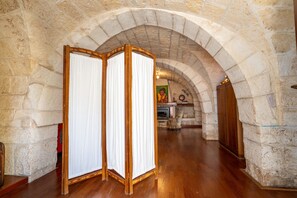 Ein gewölbter Steinkorridor mit Holzboden, einem Raumteiler und einem Kamin mit einem Porträt.