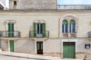 Ein Gebäude mit drei Fenstern, jeweils mit grünen Fensterläden, einem Balkon mit Geländer und einer Tür.