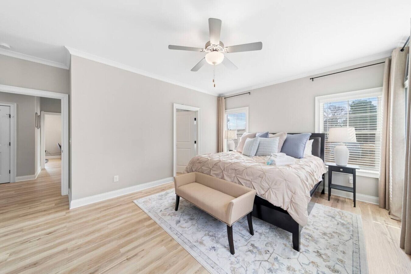 Une chambre à coucher avec un lit, un banc, un ventilateur de plafond et une fenêtre avec des stores.