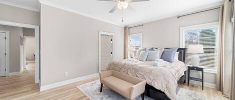 Une chambre à coucher avec un lit, un banc, un ventilateur de plafond et une fenêtre avec des stores.