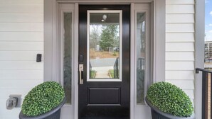 Une porte d’entrée avec le numéro « 360 » au-dessus, une porte vitrée avec une poignée, et deux plantes en pot de chaque côté.