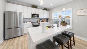 Une cuisine moderne avec des meubles blancs, des appareils en acier inoxydable, un grand îlot central doté de tabourets et une vue sur la ville par la fenêtre.