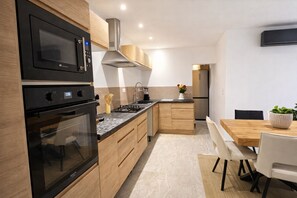 A modern kitchen with built-in appliances, wooden cabinets, and a dining area with a table and chairs. - L'Écrin Bohème 4★ – Private hot tub, pool – Montélimar (Montélimar)