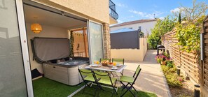 A patio with a hot tub, outdoor table, chairs, and a garden. - L'Écrin Bohème 4★ – Private Jacuzzi & Shared Pool | Cabin near P'titBonheur (Montélimar)