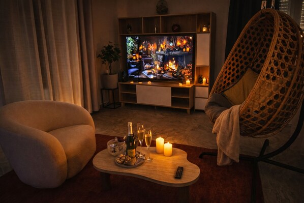 Una sala de estar acogedora con una televisión, un sillón de mimbre, un sofá, una mesa de centro con bebidas y aperitivos, y una chimenea.