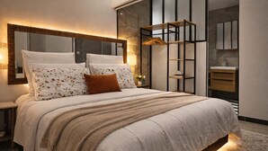 Une chambre moderne avec un grand lit, une table de chevet, une commode, un miroir, une armoire et une salle de bain équipée d’un lavabo et d’un miroir.