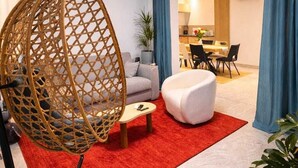 Un salon moderne avec un fauteuil suspendu, un canapé blanc, un tapis rouge et un coin repas à l’arrière-plan.
