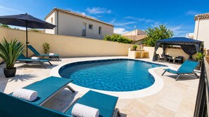 Una piscina con lettini e ombrelloni, circondata da una terrazza piastrellata.