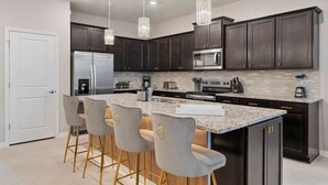 A modern kitchen with dark cabinets, stainless steel appliances, a granite countertop, and bar stools. - 8BR Villa w/ Pool & Game Room Windsor Cay (Clermont)