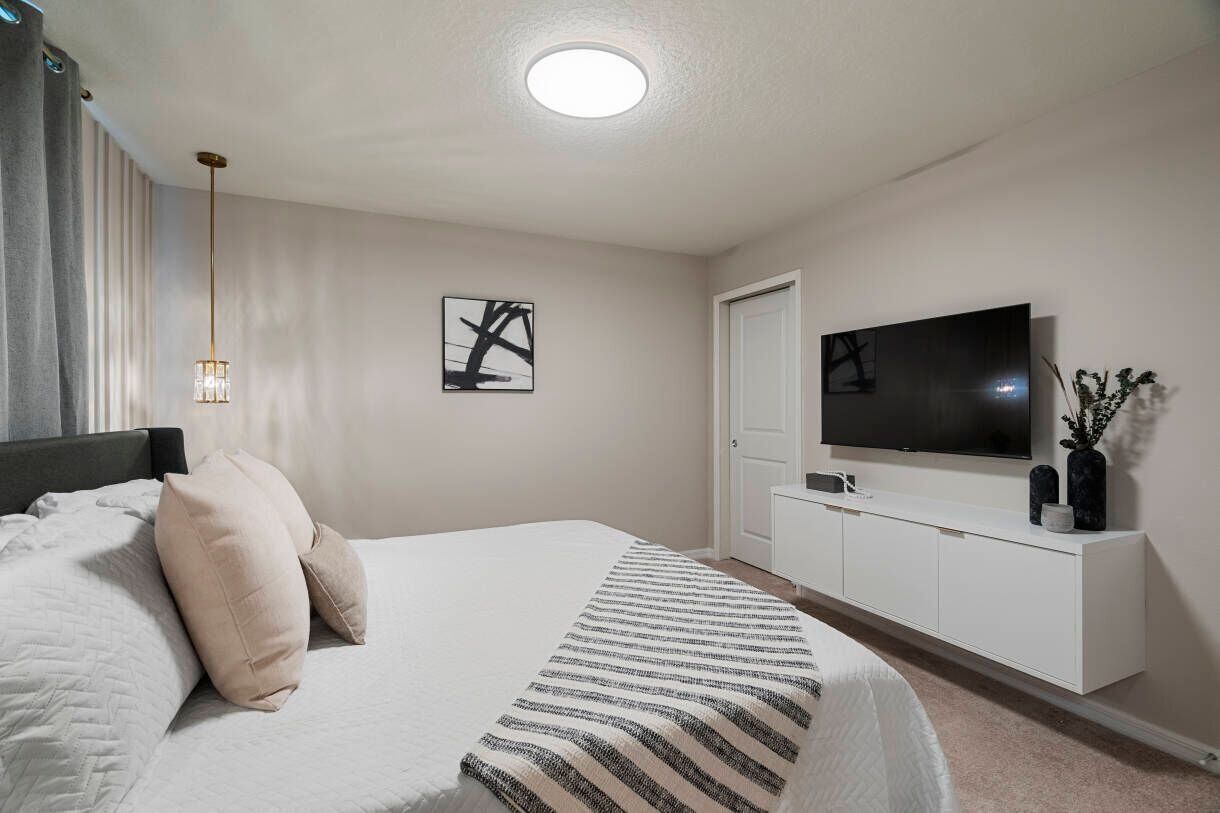 A bedroom with a bed, a TV mounted on the wall, and a bedside cabinet.