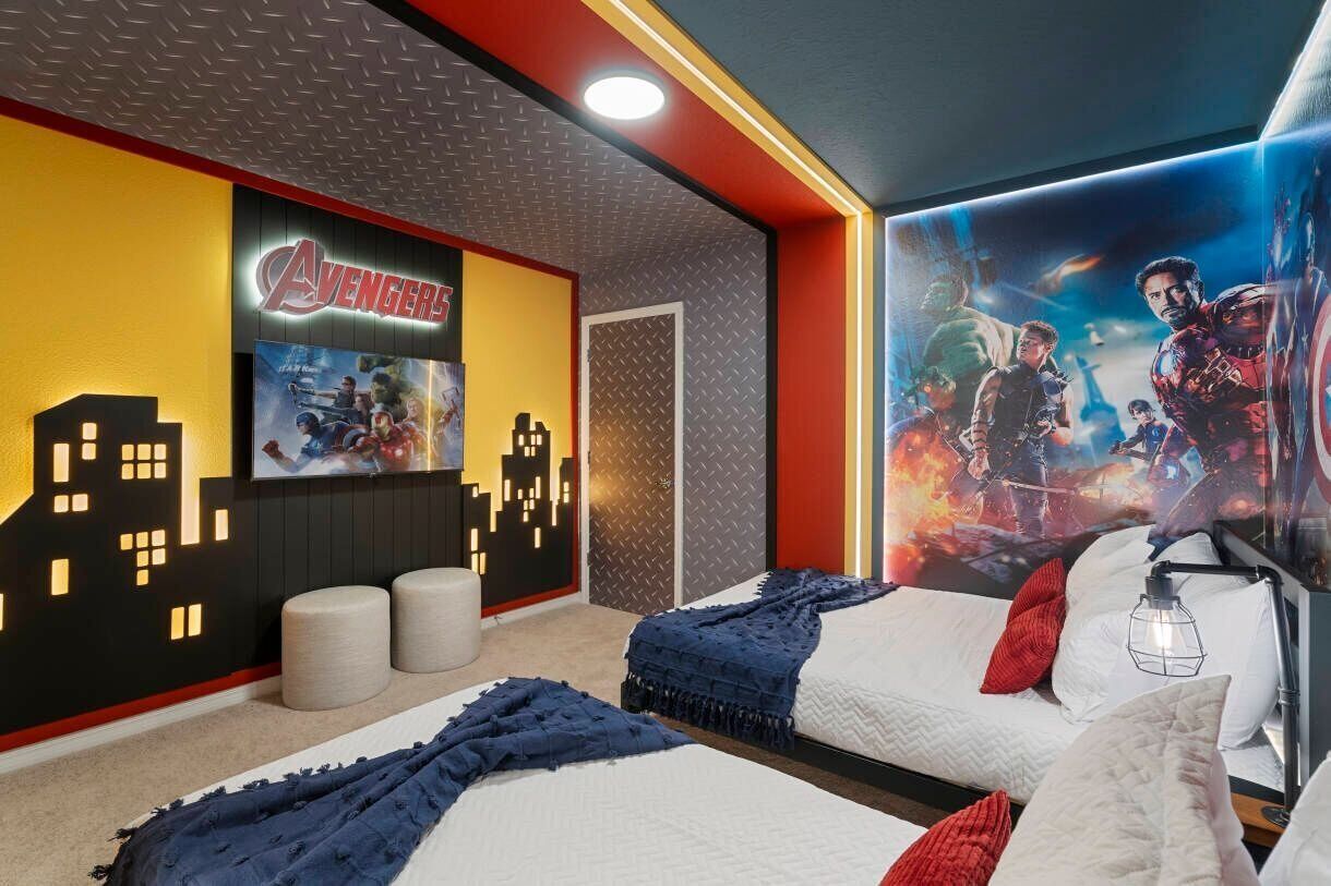 Un dormitorio con dos camas, un cuadro de arte urbano en la pared y un gran cartel de la película Vengadores.